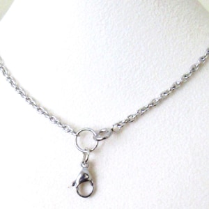 May include: A silver-toned metal chain necklace featuring a circular jump ring and a lobster claw clasp attached to the center. The chain consists of small, uniform oval links connected in a continuous pattern, creating a simple and functional design.