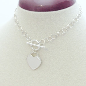 May include: A silver necklace with a heart-shaped pendant and a toggle clasp. The chain is a simple, round link style.