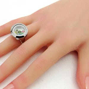 Könnte beinhalten: Ein silberner Ring mit einem Anhänger aus klarem Glas, gefüllt mit bunten Steinen.