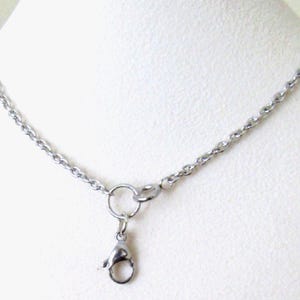 May include: A silver-colored necklace with a delicate chain design. The necklace features a lobster clasp and a small ring for attaching pendants. The chain is approximately 18 inches long.