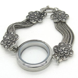 Peut inclure: Bracelet en argent avec un pendentif rond et des accents floraux. Le bracelet est composé d'une chaîne à maillons et est orné de strass scintillants.