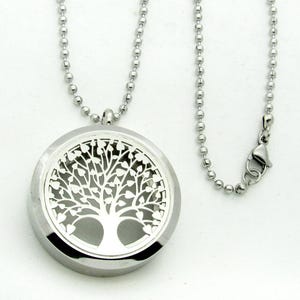 May include: A silver-toned circular locket pendant featuring a cut-out tree of life design with heart-shaped leaves. The pendant is suspended from a matching silver-toned ball chain necklace that includes a secure lobster claw clasp closure.