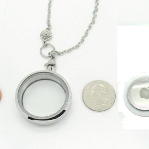 Peut inclure: Un pendentif médaillon circulaire argenté attaché à une chaîne en métal, présenté à côté d'une pièce de un cent et d'une pièce de vingt-cinq cents pour l'échelle, avec un Apple AirTag blanc portant le logo Apple sur le côté droit.