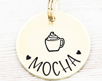 May include: Gold-colored round keychain with a black outline of a coffee cup with whipped cream and the word "MOCHA" written below it.
