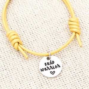 May include: A yellow leather bracelet with a silver charm that says "endo warrior" with a small heart.