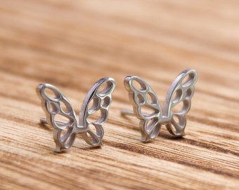 Könnte beinhalten: Ein Paar silberne Schmetterlings-Ohrringe. Die Ohrringe sind aus Metall und haben ein zartes, filigranes Design.