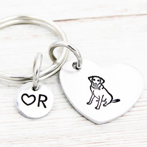 May include: Silver heart-shaped keychain with a black and white outline of a dog on one side and a silver charm with a heart and the letter R on the other side.