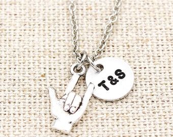 May include: Silver necklace with a hand sign charm and a round charm with the initials "T & S" engraved on it.