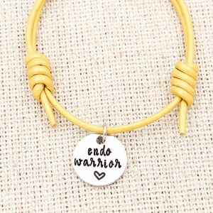 May include: A yellow leather bracelet with a silver charm that says "endo warrior" with a heart symbol.