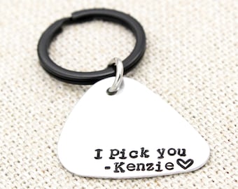 Könnte beinhalten: Ein silberner Gitarren-Plektrum-Schlüsselanhänger mit dem Text "I pick you - Kenzie" und einem kleinen Herz.