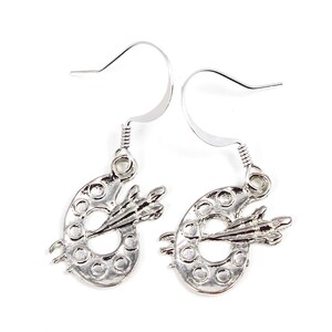 May include: Silver earrings shaped like an artist's palette with a paintbrush on top.