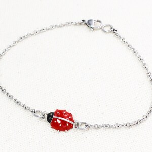 Puede incluir: Un brazalete de cadena de plata con un dije de mariquita roja.