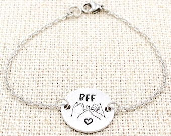 May include: Silver bracelet with a round charm that says "BFF" and has a design of two hands holding pinky fingers together with a heart in the middle.