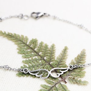 May include: A silver chain bracelet with a delicate wing charm. The bracelet has small beads along the chain.