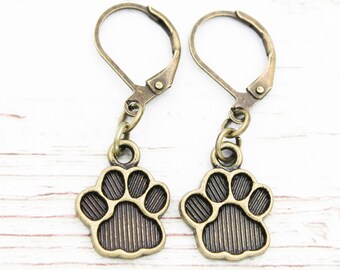 May include: A pair of bronze dangle earrings featuring a paw print design. The earrings have a leverback closure.
