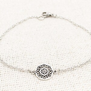 May include: A silver chain bracelet with a delicate, circular pendant featuring a detailed, intricate design.