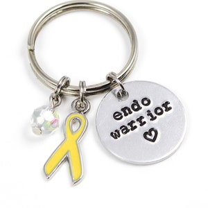 May include: A silver keychain with a yellow ribbon charm, a crystal charm, and a silver disc charm with the text "endo warrior" and a heart.