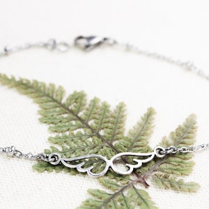 May include: A silver chain bracelet with a delicate wing charm. The bracelet has small beads along the chain.