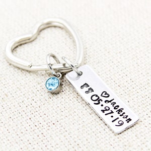 May include: Silver heart-shaped keyring with a small blue crystal charm and a rectangular tag engraved with "ft. ♥ Jackson 05.27.19".