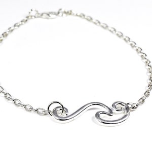 May include: A silver-colored bracelet with a chain and a decorative wave-shaped charm. The bracelet is made of a shiny metal and is displayed on a white background. The charm is a continuous, flowing design.