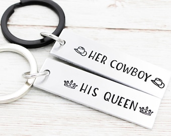 Puede incluir: Dos llaveros plateados con anillas de llaves negras. Un llavero tiene una corona y el texto "HIS QUEEN". El otro llavero tiene un sombrero de vaquero y el texto "HER COWBOY".