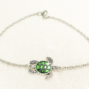 May include: A silver chain bracelet with a green turtle charm. The turtle is detailed with a textured shell and has a silver outline.
