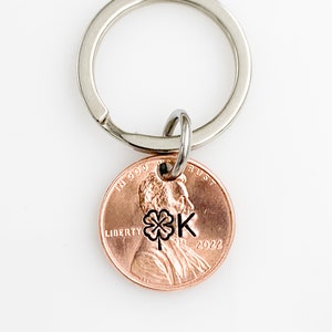 May include: A silver key chain with a 2022 penny attached. The penny has a four-leaf clover and the letter "K" engraved on it.