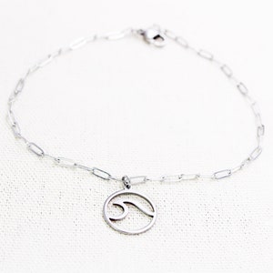 May include: A silver chain anklet with a silver wave charm. The chain is made of small, linked circles.
