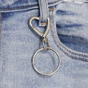 May include: A silver heart-shaped keychain with a round ring attached to a pair of light blue denim jeans.