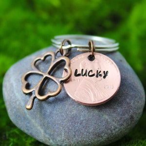 May include: A copper penny keychain with a four-leaf clover charm and the word "LUCKY" engraved on the coin. The coin is dated 2019.