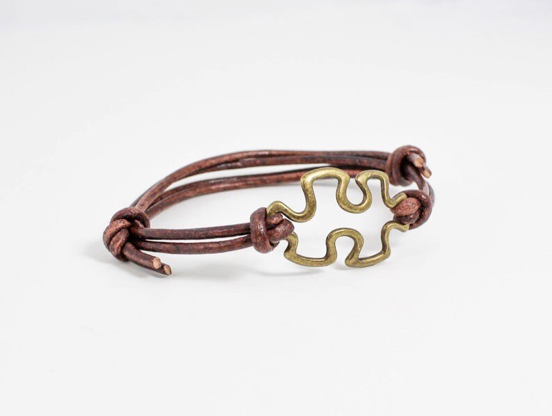 May include: A brown leather bracelet with a gold-toned puzzle piece charm.