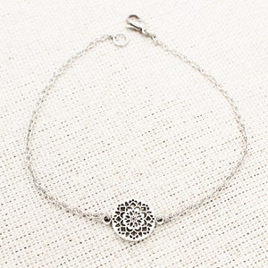 May include: A silver chain bracelet with a delicate, circular pendant featuring a cutout design.