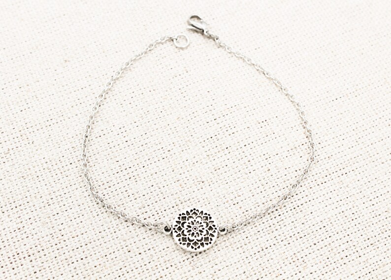 May include: A silver chain bracelet with a delicate, circular pendant featuring a cutout design.