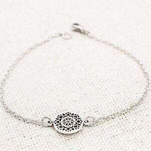 May include: A silver chain bracelet with a delicate, circular pendant featuring a cutout mandala design.