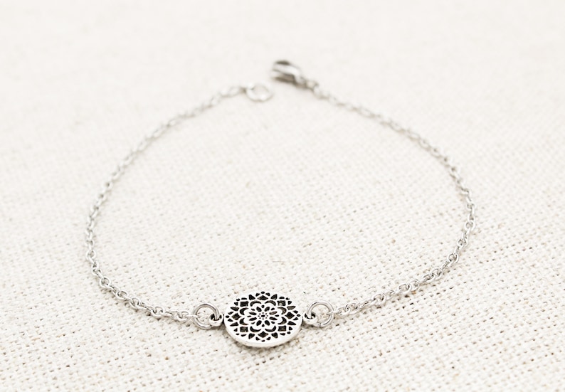 May include: A silver chain bracelet with a delicate, circular pendant featuring a cutout mandala design.