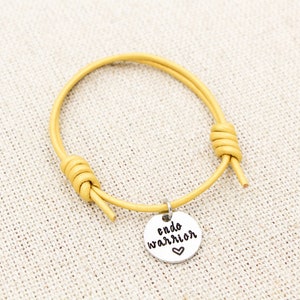 May include: A yellow leather bracelet with a silver charm that says "endo warrior" with a heart symbol.
