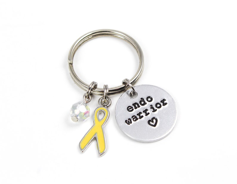 May include: A silver keychain with a yellow ribbon charm, a crystal charm, and a silver disc charm with the text "endo warrior" and a heart.