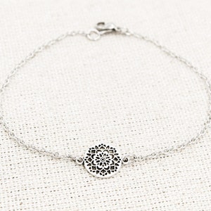 May include: A silver chain bracelet with a delicate, circular pendant featuring a filigree design.