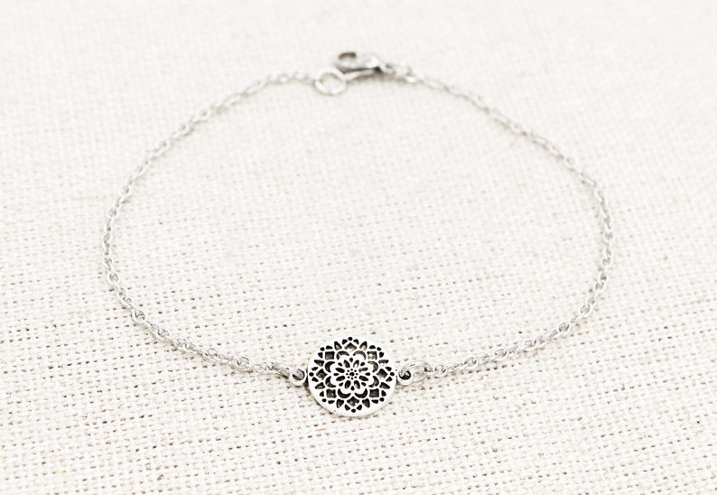 May include: A silver chain bracelet with a delicate, circular pendant featuring a filigree design.