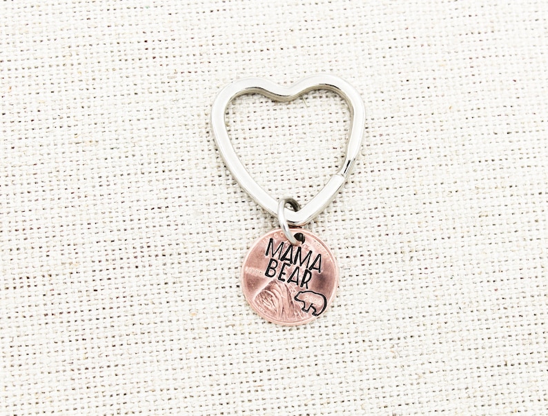 May include: A silver heart-shaped keychain with a copper penny charm that reads "Mama Bear" with a small bear silhouette.