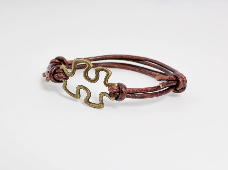 May include: A brown leather bracelet with a gold-toned puzzle piece charm.