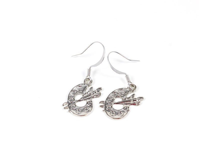 May include: Silver dangle earrings featuring a paint palette with a paintbrush design.