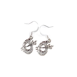 May include: Silver dangle earrings featuring a small paint palette with a paintbrush design.