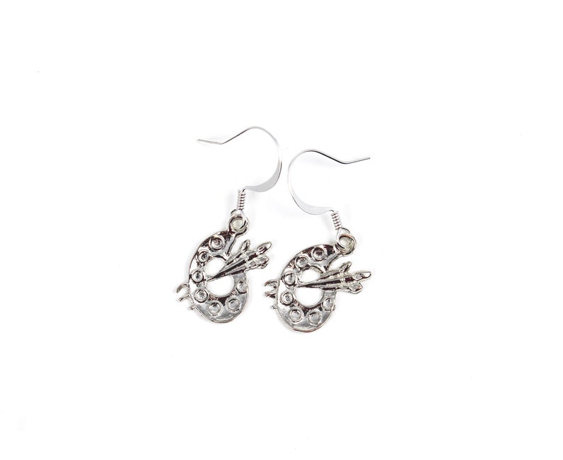 May include: Silver dangle earrings featuring a small paint palette with a paintbrush design.