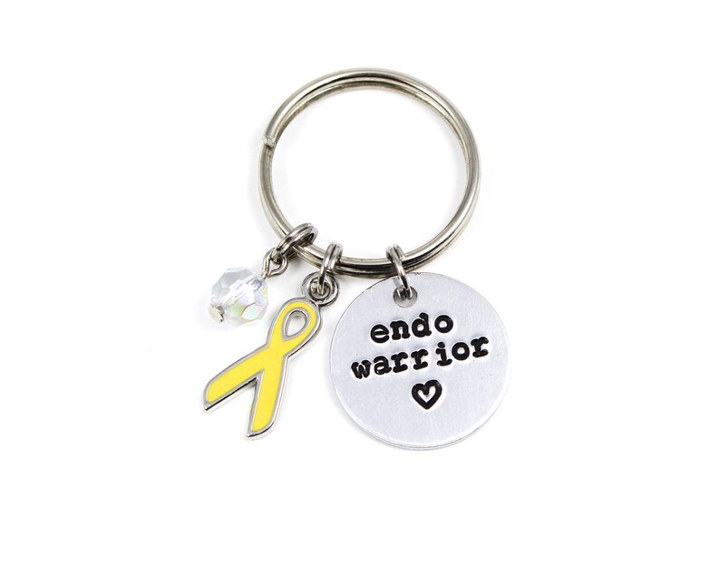May include: A silver keychain with a yellow ribbon charm, a crystal charm, and a round silver charm with the text "endo warrior" and a small heart.