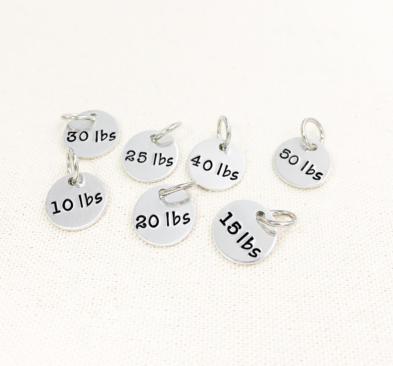 May include: Seven silver metal weight markers with key rings. The markers are round and have the following weights printed on them: 10 lbs, 15 lbs, 20 lbs, 25 lbs, 30 lbs, 40 lbs, and 50 lbs.