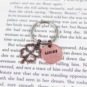 May include: A silver key chain with a copper four-leaf clover charm and a copper penny with the word "LUCKY" stamped on it.