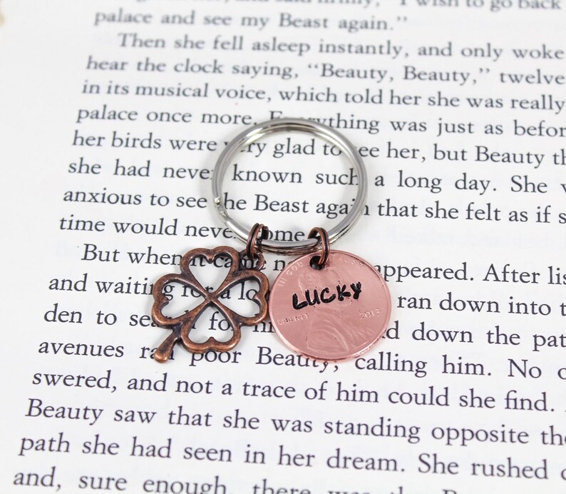May include: A silver key chain with a copper four-leaf clover charm and a copper penny with the word "LUCKY" stamped on it.