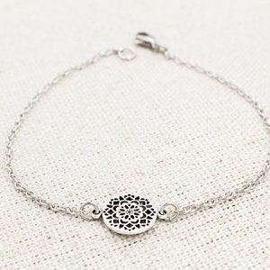 May include: A silver chain bracelet with a delicate, circular pendant featuring a detailed, intricate design.