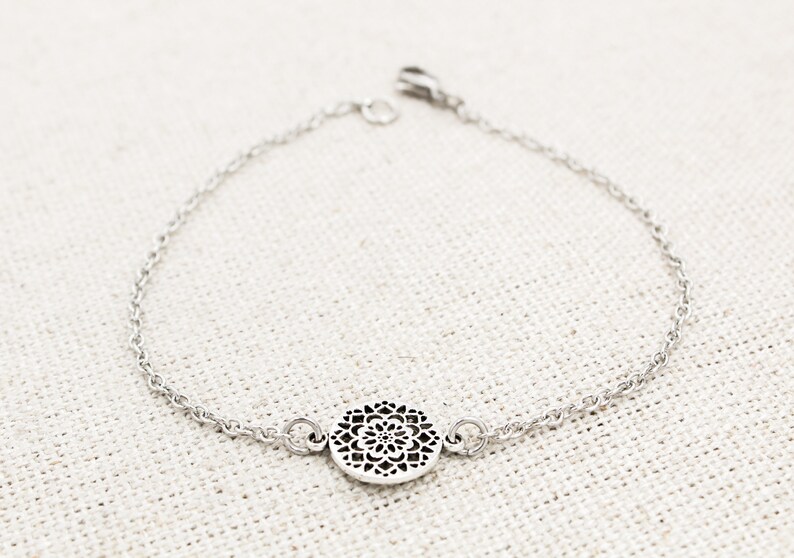 May include: A silver chain bracelet with a delicate, circular pendant featuring a detailed, intricate design.